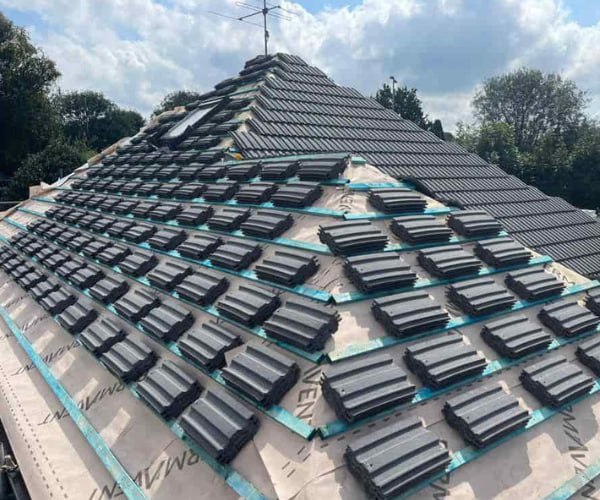 This is a photo of a new hip roof being installed. New felt, battens, and grey tiles have been installed, also a new velux window. Works carried out by SCG Roofing Earls Barton