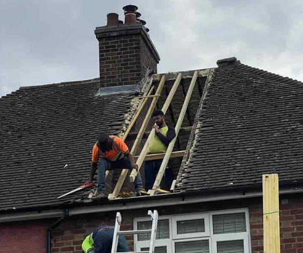 This is a photo of a roof repair being carried out. A section of the roof has been stripped and two roofers are replacing the rafters. Works being carried out by SCG Roofing Earls Barton